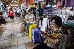 Một người phụ nữ đang sử dụng điện thoại di động trong khu chợ đông đúc, tượng trưng cho sự tương tác số trong đời sống hàng ngày.