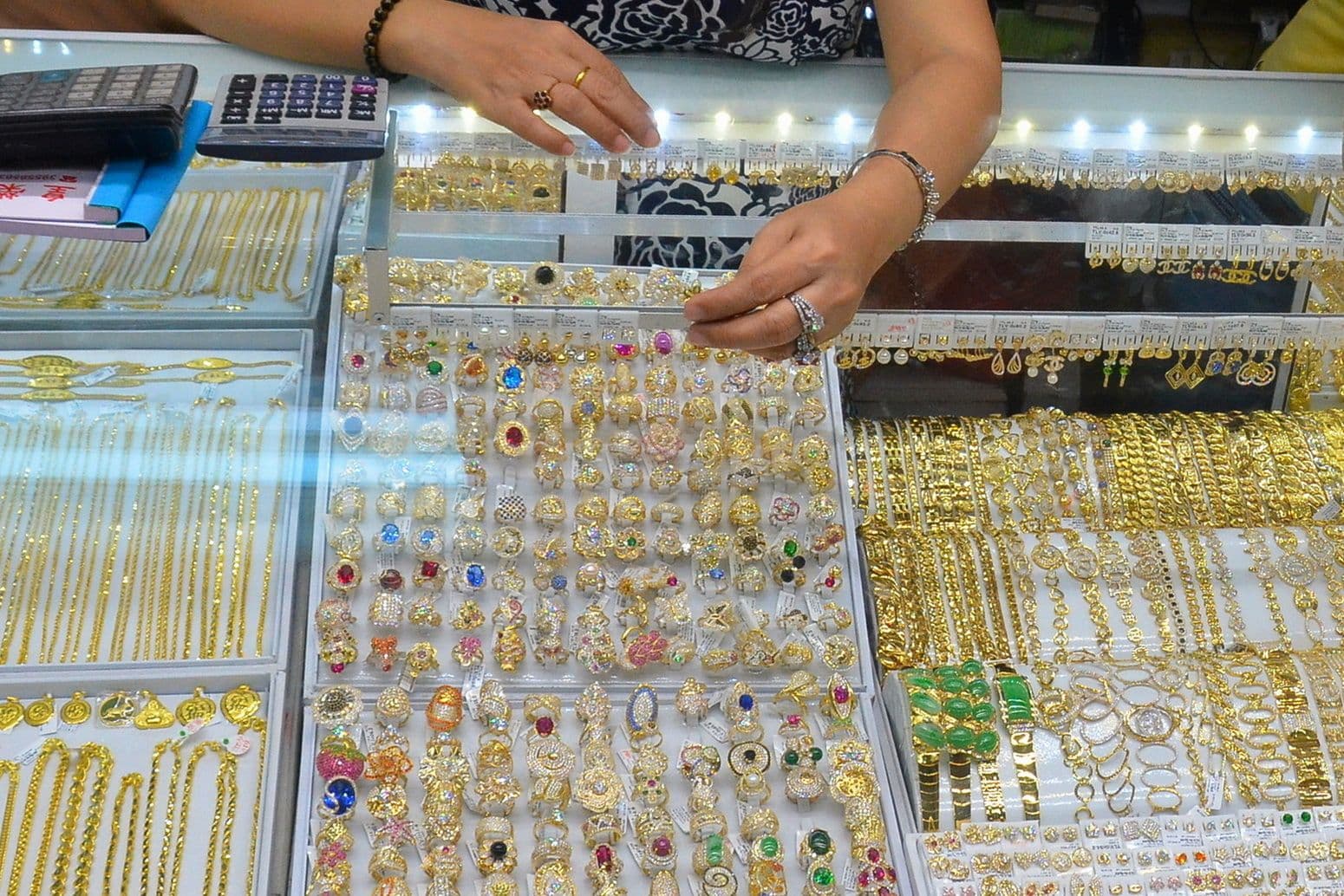 Một người phụ nữ đang xem xét các loại trang sức vàng đa dạng trong cửa hàng, phản ánh thị trường vàng sôi động.