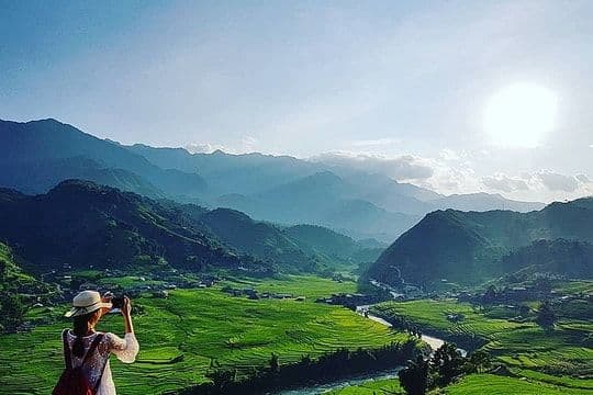 Một người phụ nữ chụp ảnh phong cảnh núi non hùng vĩ với ruộng bậc thang xanh tươi, tượng trưng cho trải nghiệm du lịch trong kỳ nghỉ lễ.