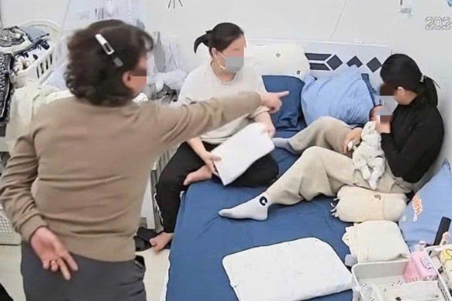 Một người phụ nữ lớn tuổi đang mắng mỏ một người phụ nữ trẻ đang bế em bé trên giường, thể hiện mâu thuẫn mẹ chồng nàng dâu sau sinh.