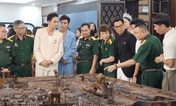 Một nhóm người, bao gồm nghệ sĩ và quân nhân, xem sa bàn mô phỏng phim trường lịch sử, thể hiện sự quan tâm đến di sản dân tộc.