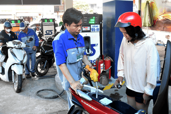 Một nhân viên đang đổ xăng cho xe máy tại trạm xăng, thể hiện sự điều chỉnh giá xăng dầu và tác động đến người tiêu dùng.