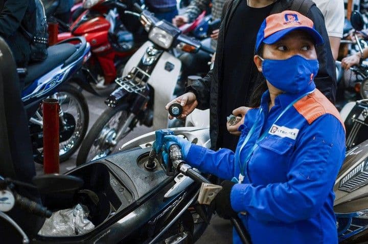 Một nhân viên đang đổ xăng vào xe máy tại trạm xăng, minh họa cho giá xăng và tác động đến người tiêu dùng.