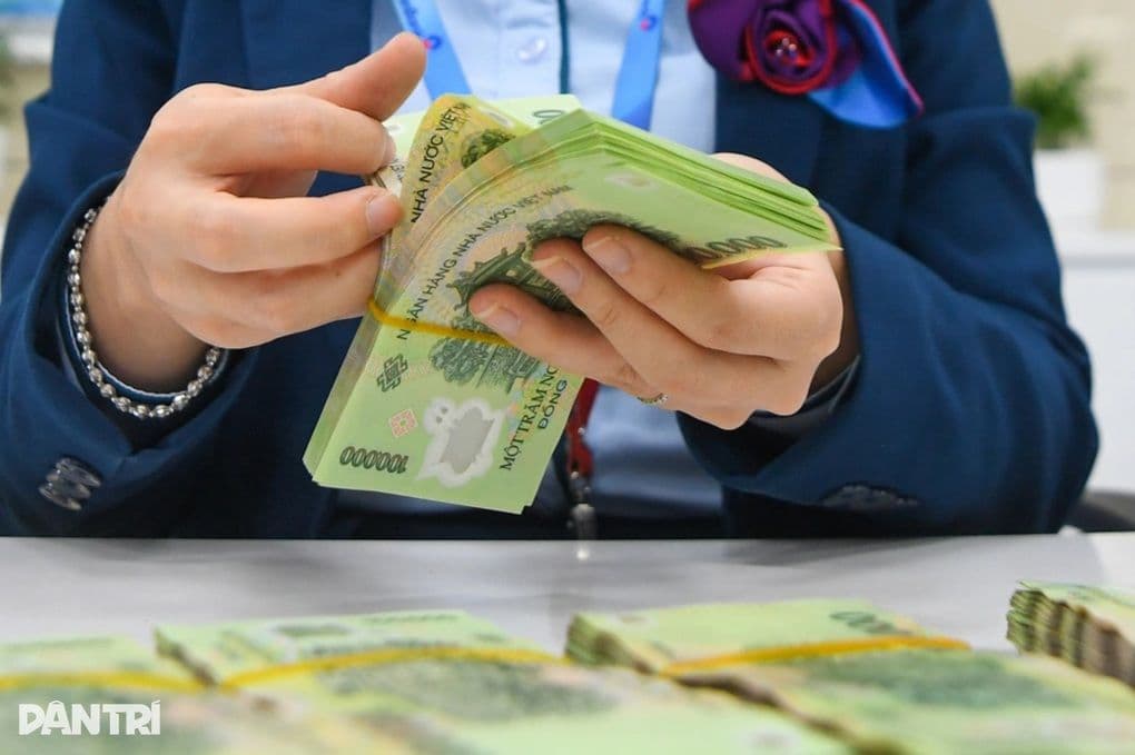 Một nhân viên ngân hàng đang đếm các tờ tiền 100.000 đồng, tượng trưng cho việc chi trả các khoản an sinh xã hội.