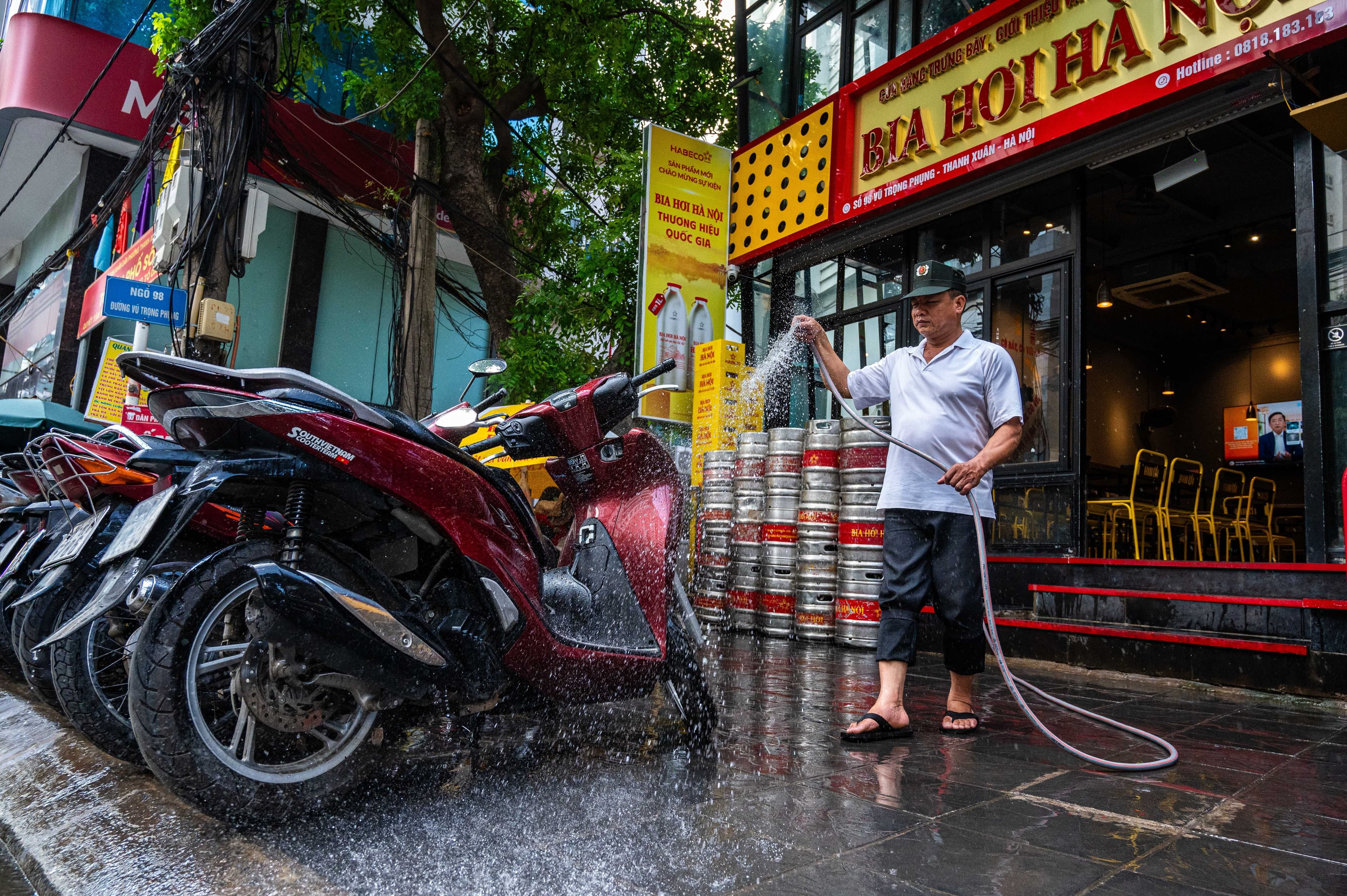Một nhân viên nhà hàng xịt nước làm mát vỉa hè và xe máy tại Hà Nội, thể hiện 'cuộc chiến thầm lặng' chống chọi nắng nóng.