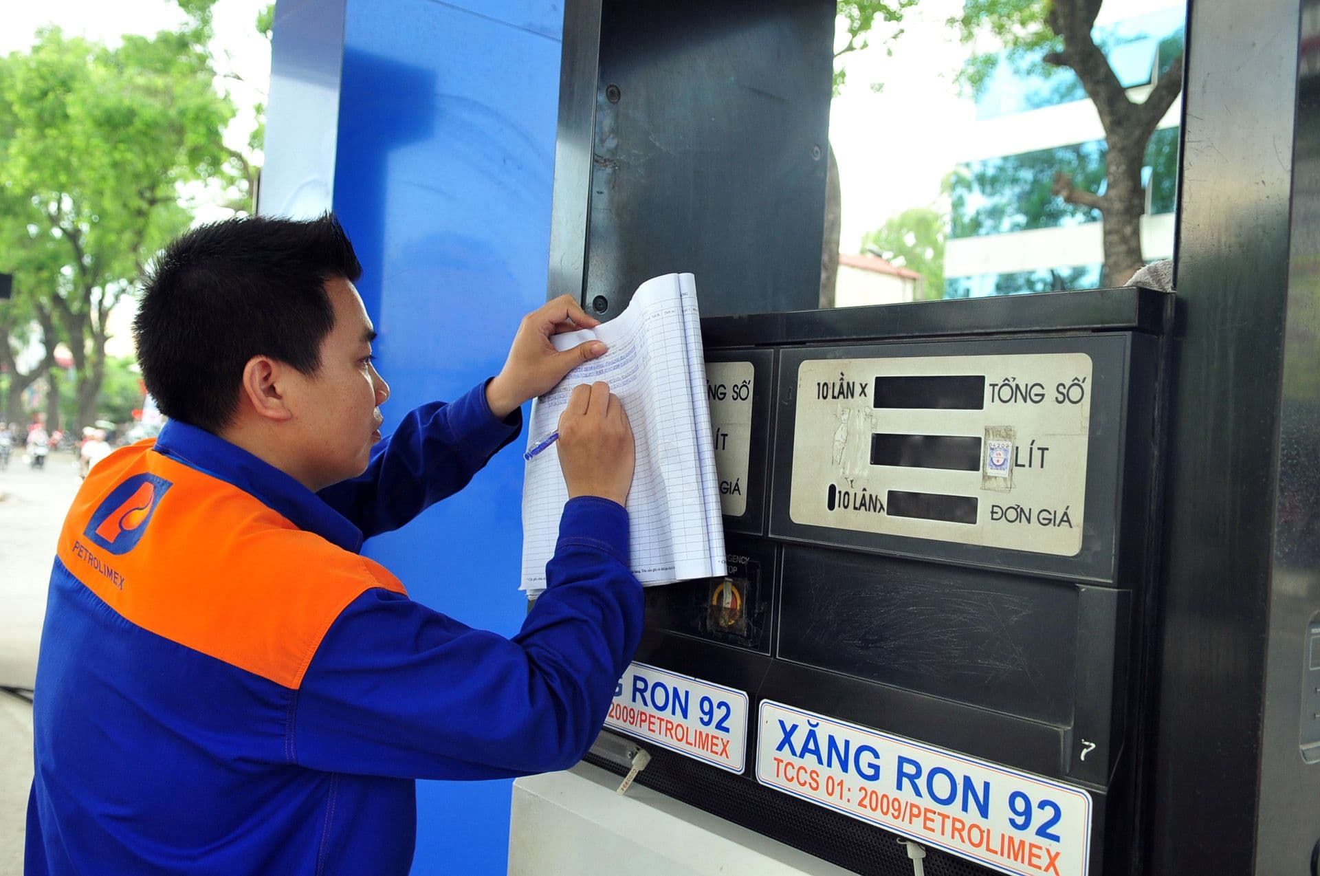 Một nhân viên Petrolimex đang ghi chép thông tin hoặc điều chỉnh bảng giá tại cột bơm xăng, thể hiện sự biến động và quản lý giá xăng dầu.