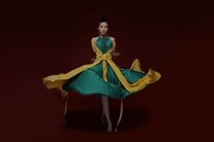 Một phụ nữ mặc váy xanh vàng cách điệu, đang tạo dáng nghệ thuật, tượng trưng cho sự sáng tạo và tư duy mới trong nhạc Tết của nghệ sĩ trẻ.