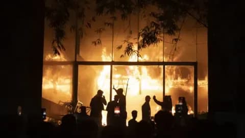 Một tòa nhà đang bốc cháy dữ dội vào ban đêm, với những bóng người đứng nhìn từ xa. Hình ảnh này tượng trưng cho các cuộc tấn công bạo lực và khủng bố mà Pakistan đang đối mặt.