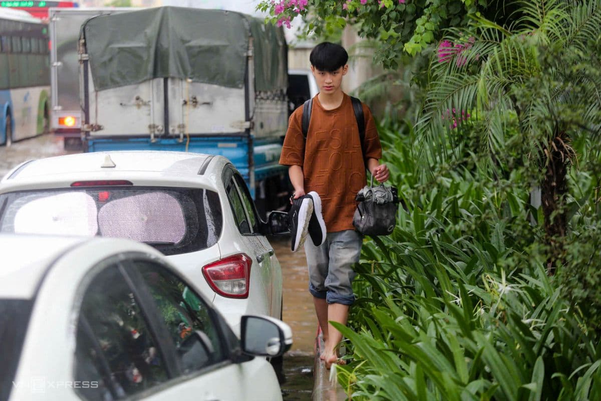 Một thanh niên lội bộ chân trần, mang giày trên tay qua đoạn đường ngập nước ở Hà Nội, thể hiện tinh thần kiên cường của người dân.
