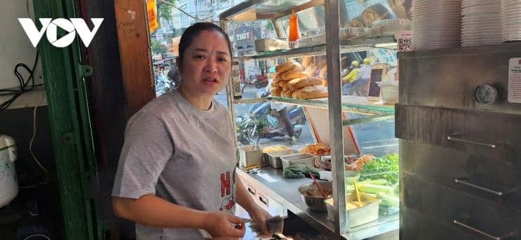 Một tiểu thương đứng bán hàng tại quầy, gương mặt lo lắng, thể hiện áp lực giữ giá bán lẻ dù chi phí đầu vào tăng cao.