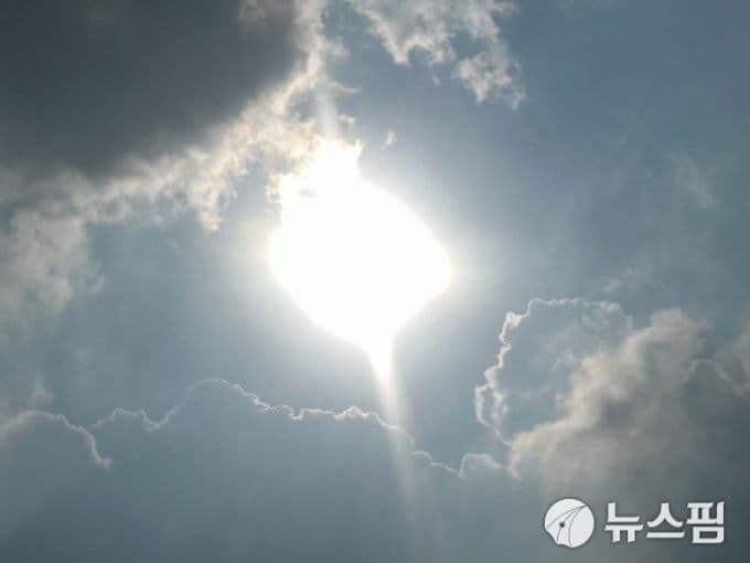 Mặt trời chói chang xuyên qua những đám mây, tượng trưng cho nắng gắt và sự biến đổi của khí hậu.