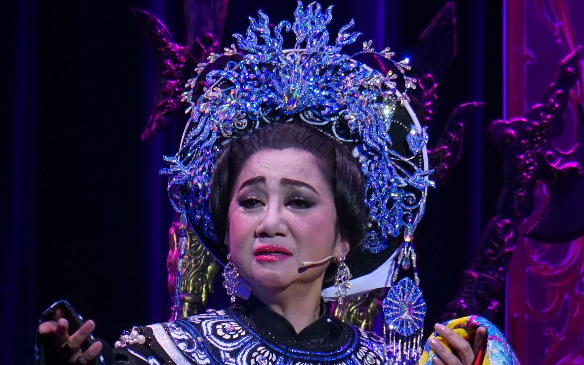 Nữ nghệ sĩ cải lương biểu diễn đầy cảm xúc trên sân khấu với trang phục và mũ đội đầu truyền thống lộng lẫy