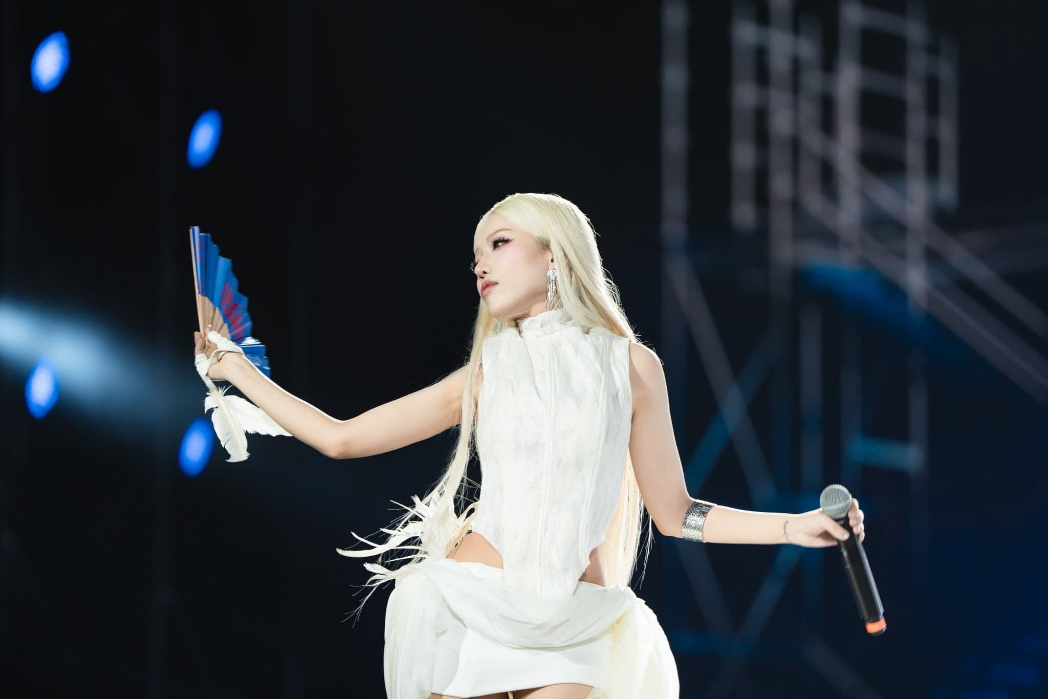 Nữ nghệ sĩ trẻ với mái tóc bạch kim và trang phục hiện đại màu trắng biểu diễn trên sân khấu lớn, tượng trưng cho tinh thần khởi động, sự bứt phá và bản sắc mới mà nhạc Xuân hiện đại gửi gắm.