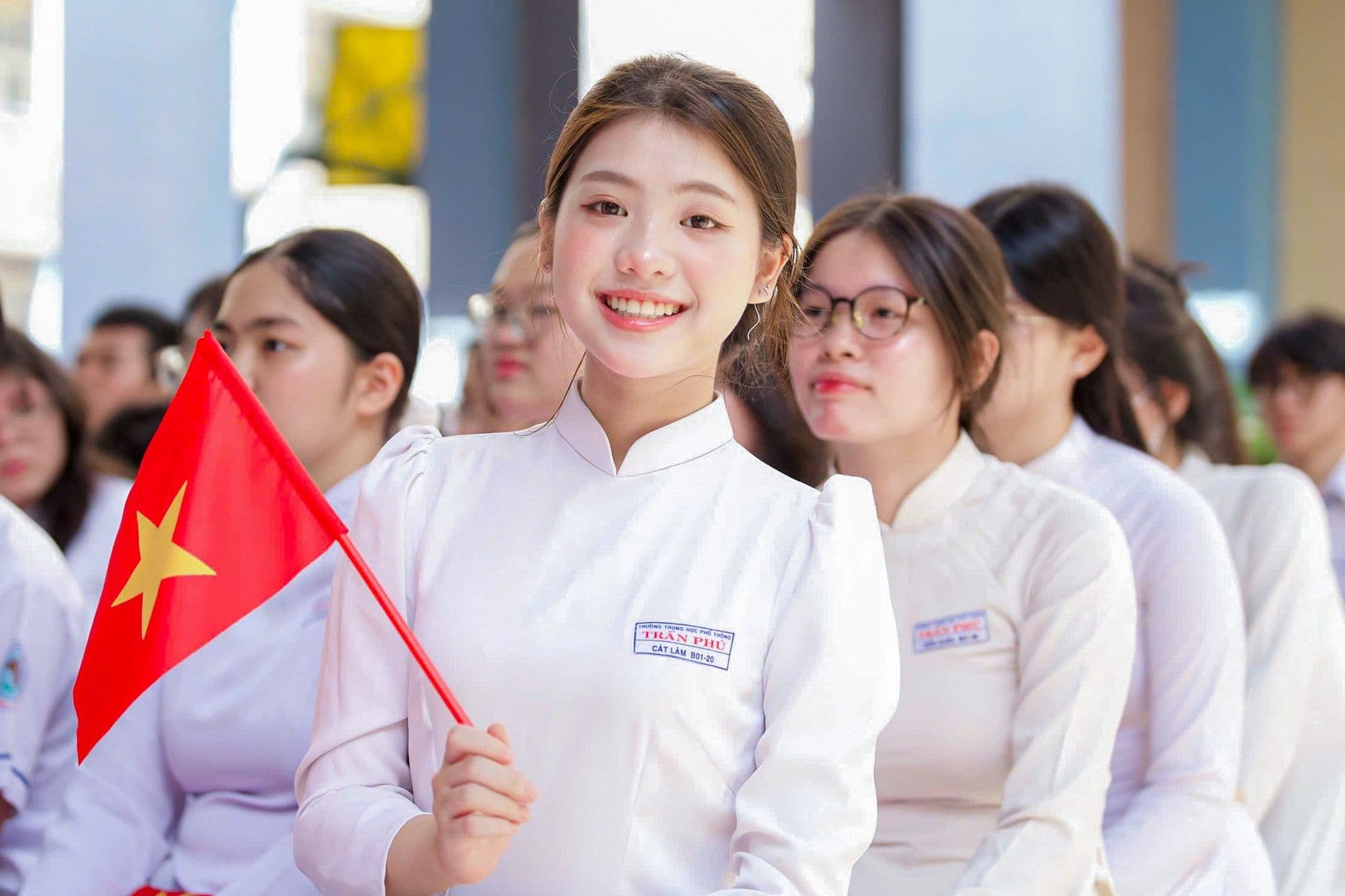 Nữ sinh Việt Nam trong tà áo dài trắng tươi cười cầm cờ, tượng trưng cho lòng tri ân của học trò nhân ngày Nhà giáo Việt Nam 20/11.