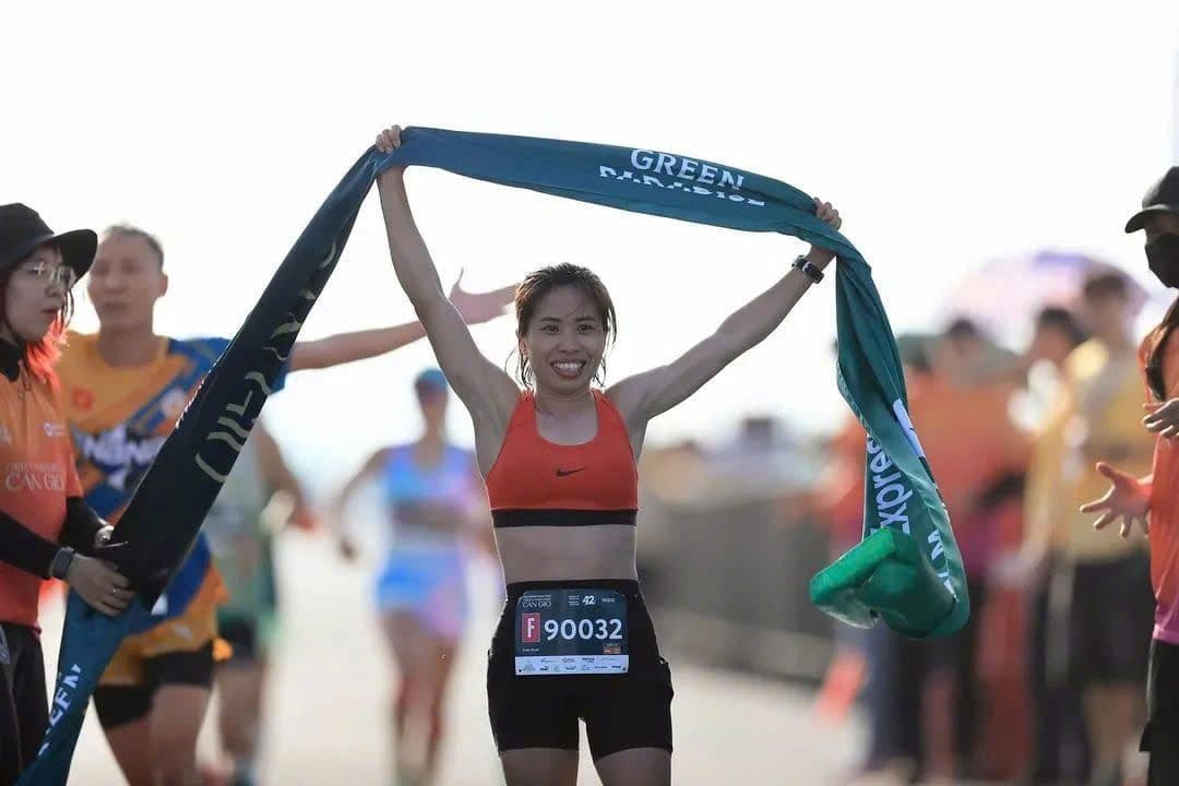 Nữ vận động viên marathon vui mừng giơ cao băng rôn 'Green Paradise' sau khi hoàn thành cuộc đua, tượng trưng cho lối sống khỏe mạnh tại Vinhomes Cần Giờ.
