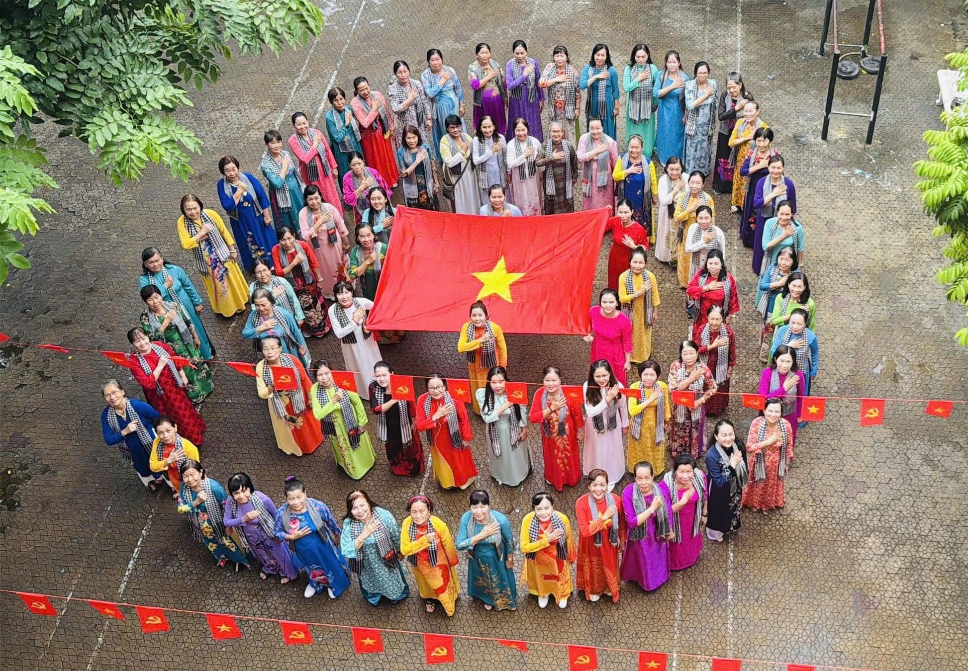 Đông đảo phụ nữ trong trang phục áo dài truyền thống cùng nhau cầm cờ Tổ quốc, biểu tượng của tình đoàn kết và khát vọng vươn lên