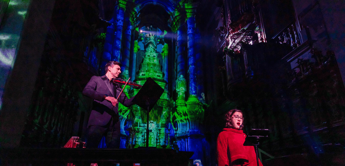 Nghệ sĩ biểu diễn violin và ca sĩ trong nhà thờ Clérigos được chiếu sáng bằng hình ảnh 360 độ xanh lá và xanh dương, minh họa sự kiện 'Spiritus Vitae'.