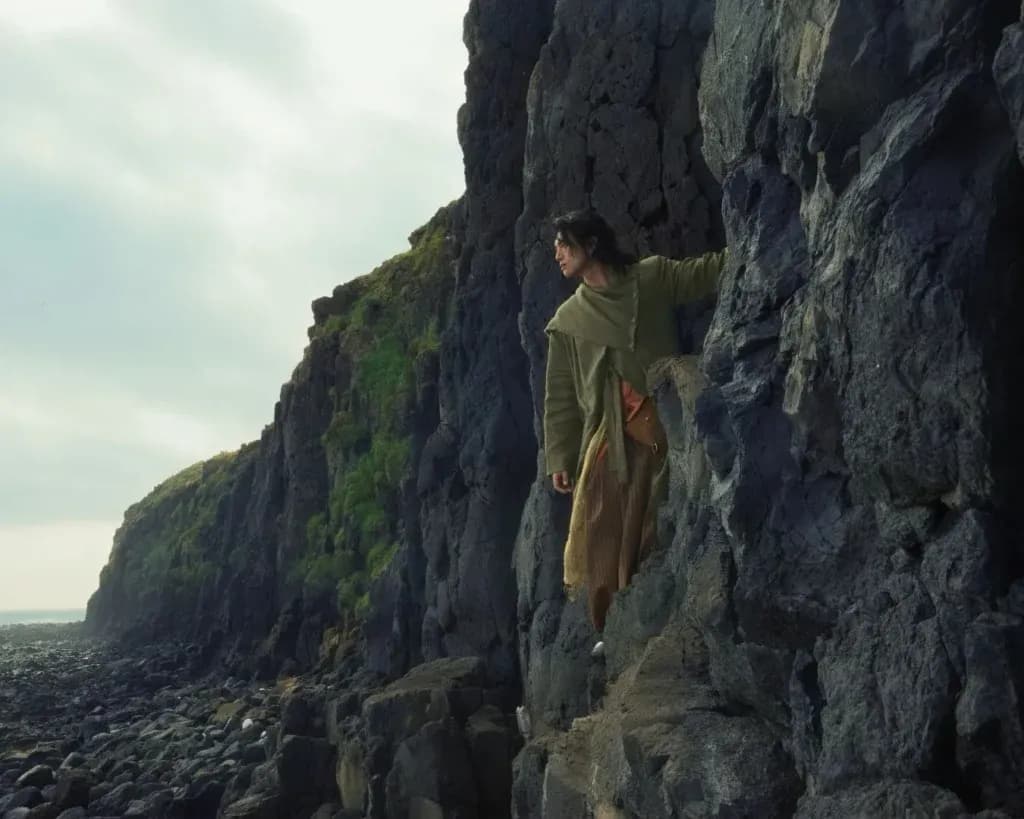 Nghệ sĩ GREY D leo lên vách đá, thể hiện nỗ lực của nghệ sĩ trong việc tìm chỗ đứng giữa sự phức tạp và méo mó của bảng xếp hạng kỹ thuật số.