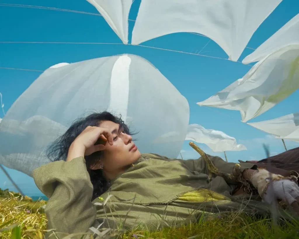 Nghệ sĩ GREY D nằm giữa cánh đồng với những tấm vải trắng bay lượn, tượng trưng cho sự tự do và hy vọng về một tương lai âm nhạc đề cao giá trị thật.