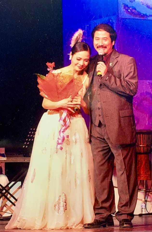 Nghệ sĩ Lê Vi trên sân khấu cùng một người thầy, tượng trưng cho di sản tinh thần từ những người đã định hướng tâm hồn cô.