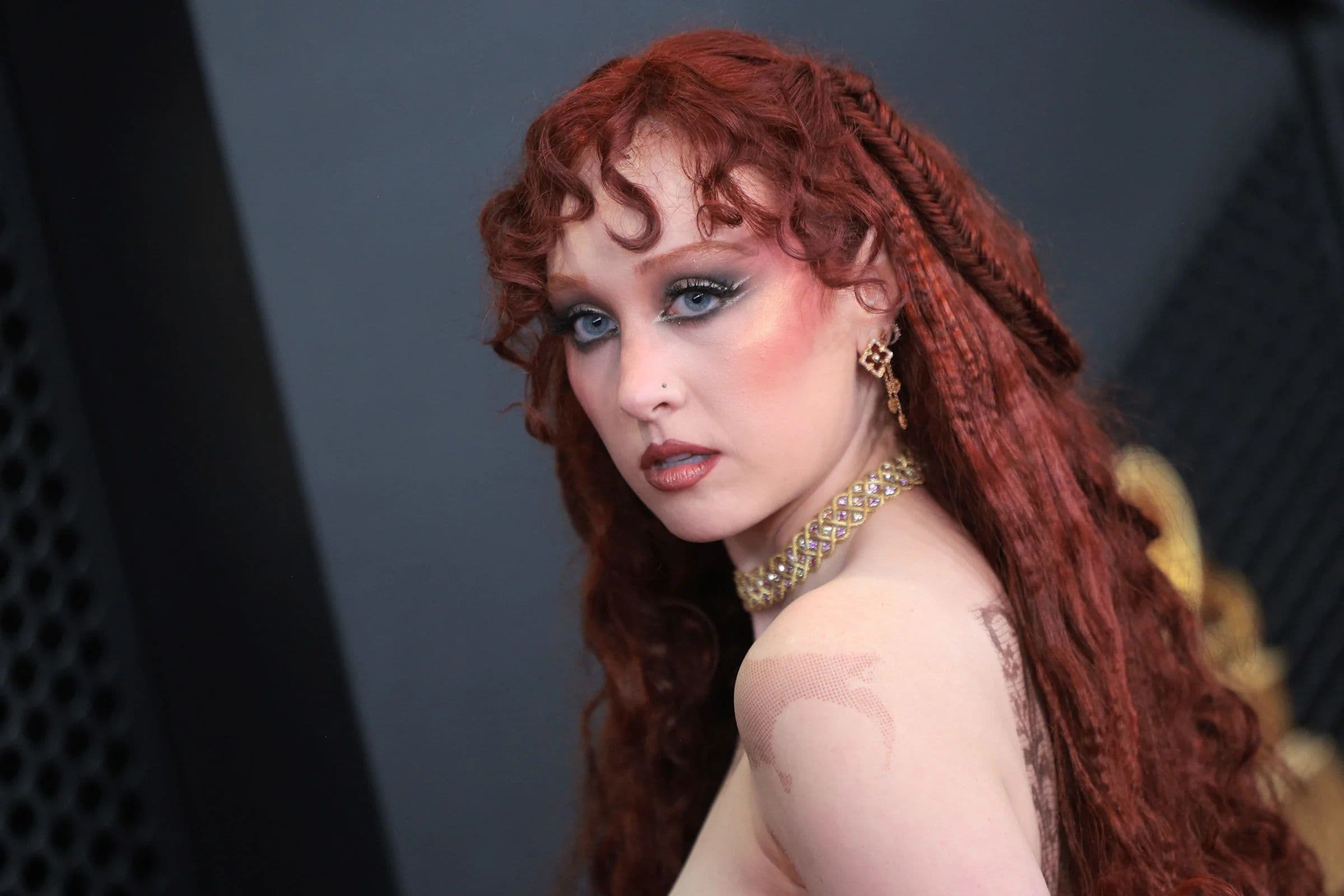 Nghệ sĩ với mái tóc đỏ xoăn và trang điểm ấn tượng tại Grammy 2026, tượng trưng cho những bất ngờ của mùa giải.