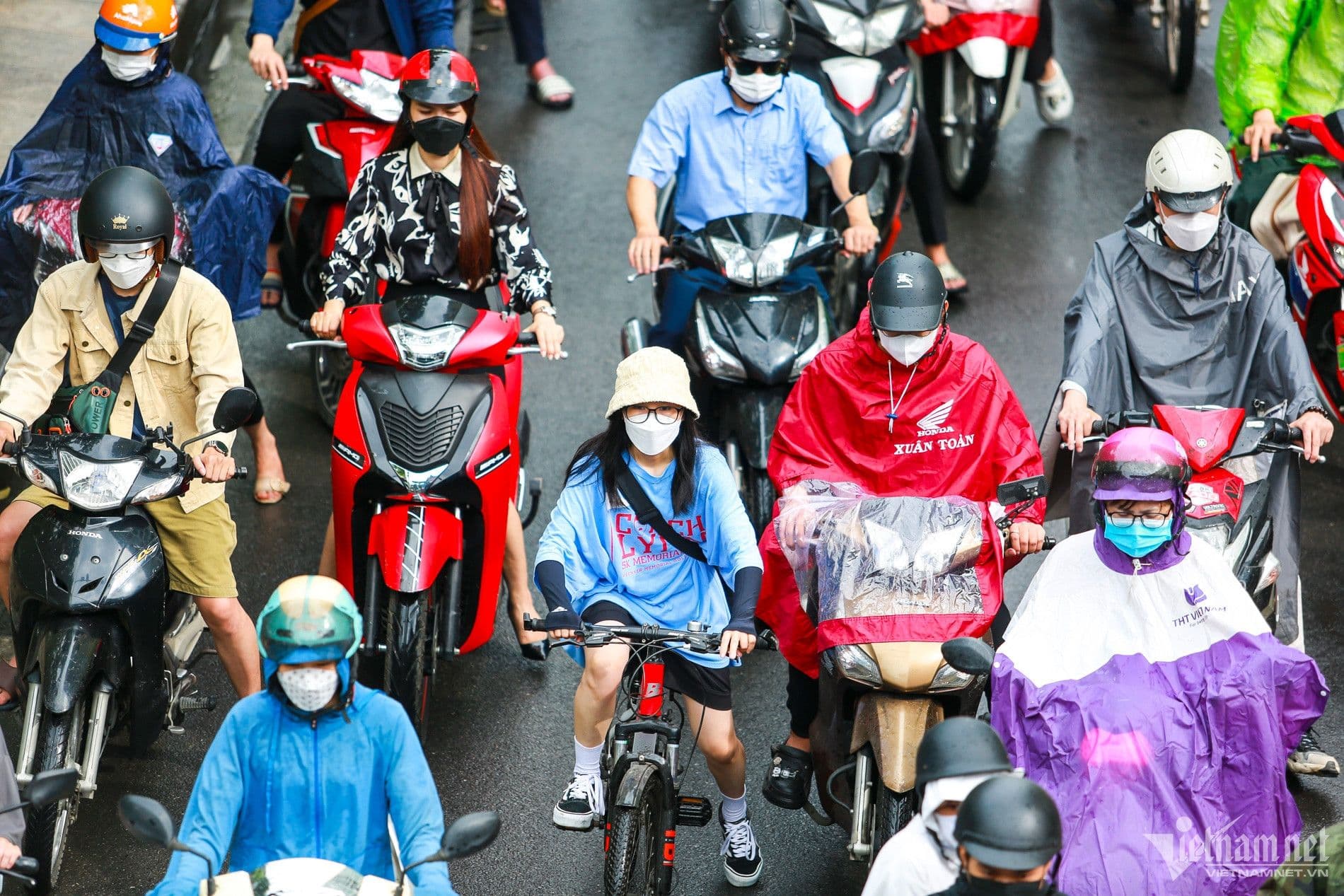 Người dân di chuyển trên đường phố, một số mặc áo mưa, phản ánh sự ảnh hưởng của dự báo thời tiết đến hoạt động hàng ngày.