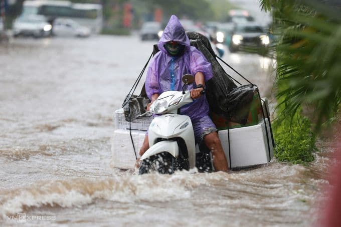 Người dân Hà Nội di chuyển khó khăn trên xe máy chất đầy hàng hóa qua đường ngập sâu sau trận mưa lớn.