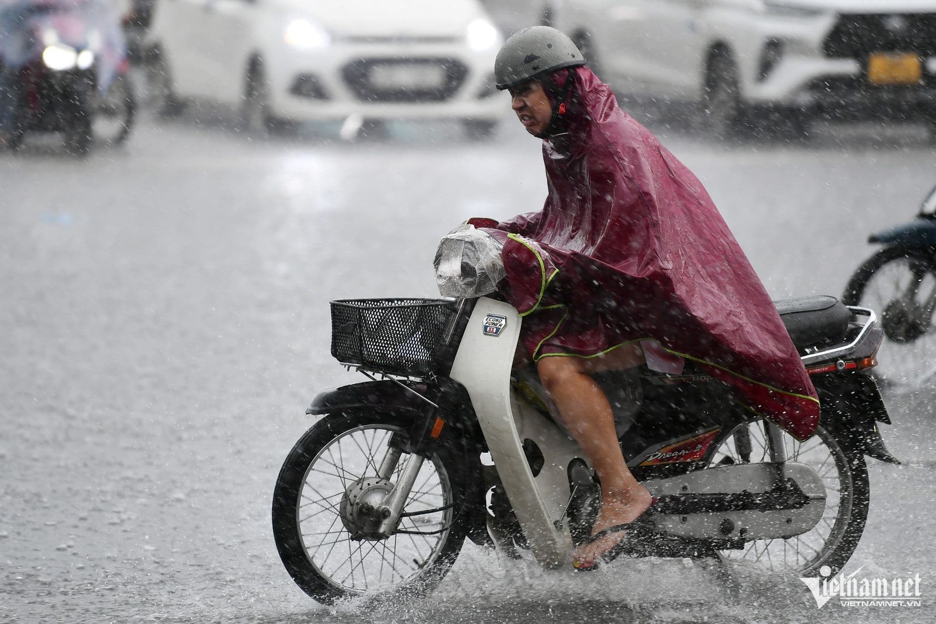 Người dân Hà Nội đi xe máy trong mưa lớn, nước bắn tung tóe trên đường phố.