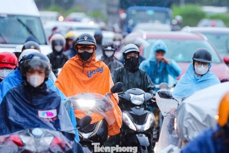 Người dân Hà Nội mặc áo mưa di chuyển trên đường phố trong điều kiện mưa dông.