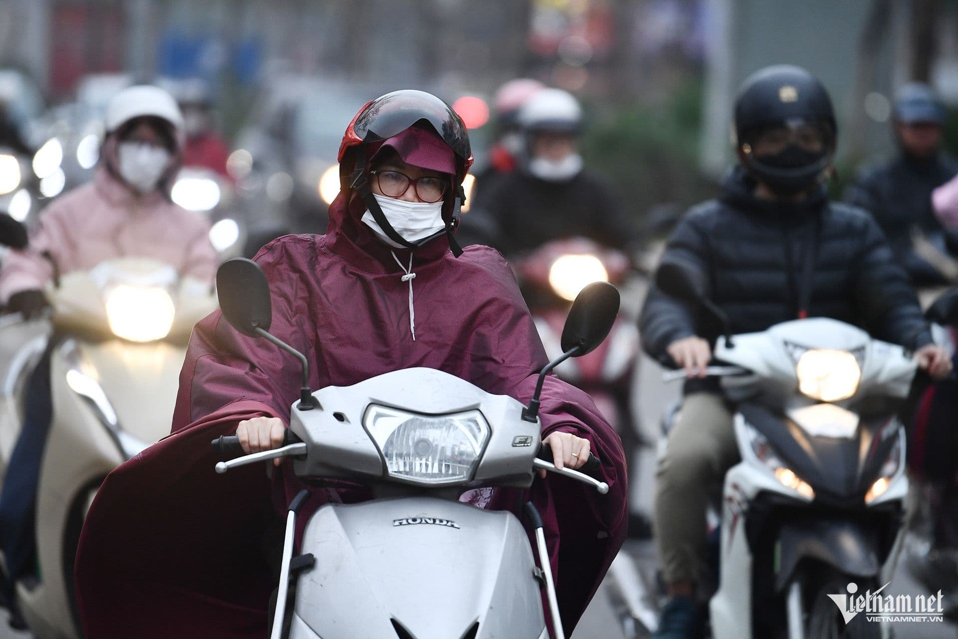 Người dân Hà Nội mặc áo mưa, đeo khẩu trang di chuyển trên xe máy trong thời tiết rét đậm, mưa phùn.