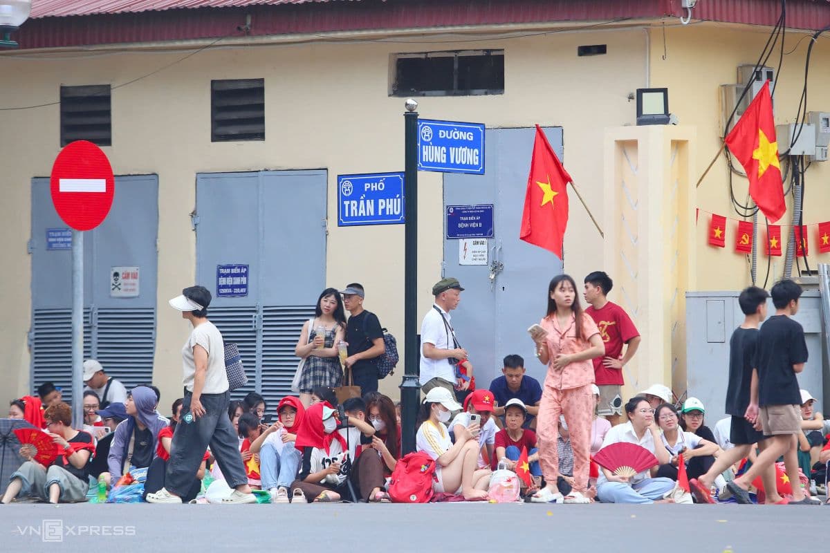 Người dân Hà Nội ngồi chờ trên vỉa hè gần biển báo đường Hùng Vương và Trần Phú, chuẩn bị xem diễu binh.