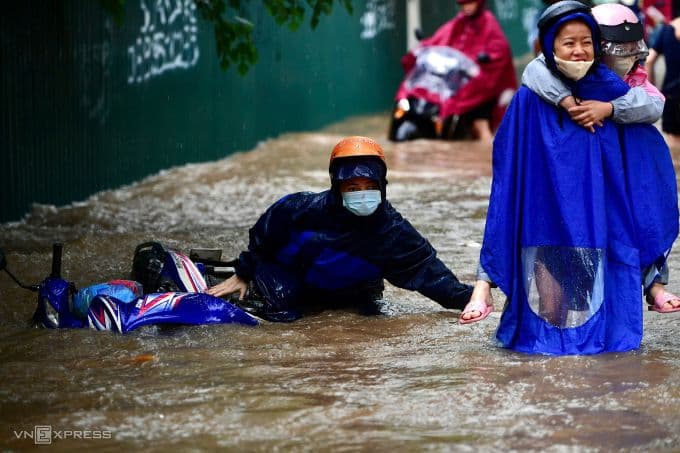 Người dân Hà Nội vật lộn giữa dòng nước ngập sâu sau mưa lớn, một xe máy bị đổ trên phố.