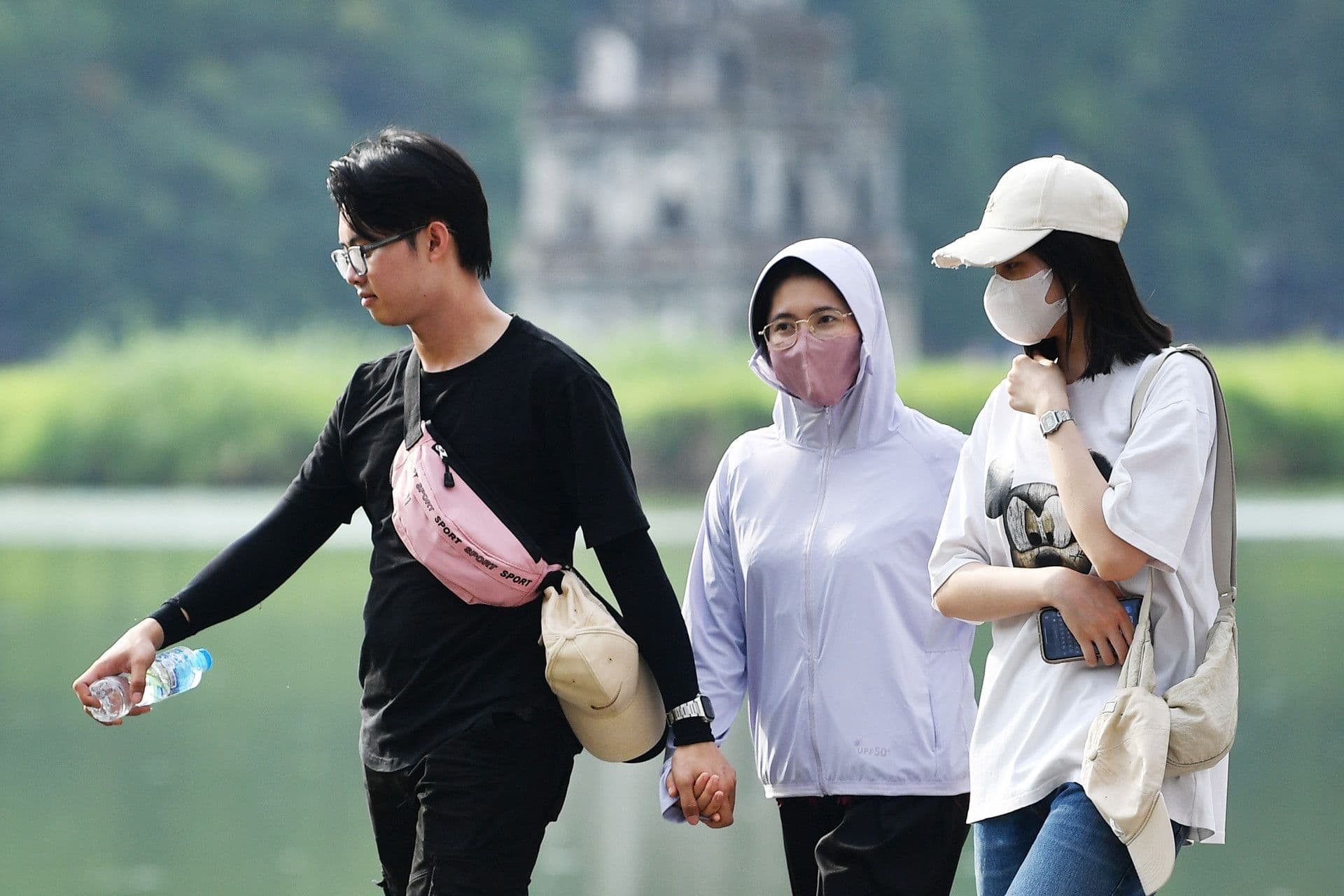 Người dân đi bộ dưới trời nắng, một số che chắn hoặc mặc áo khoác, thể hiện sự giao thoa giữa hơi lạnh và nắng nóng sớm ở miền Bắc.