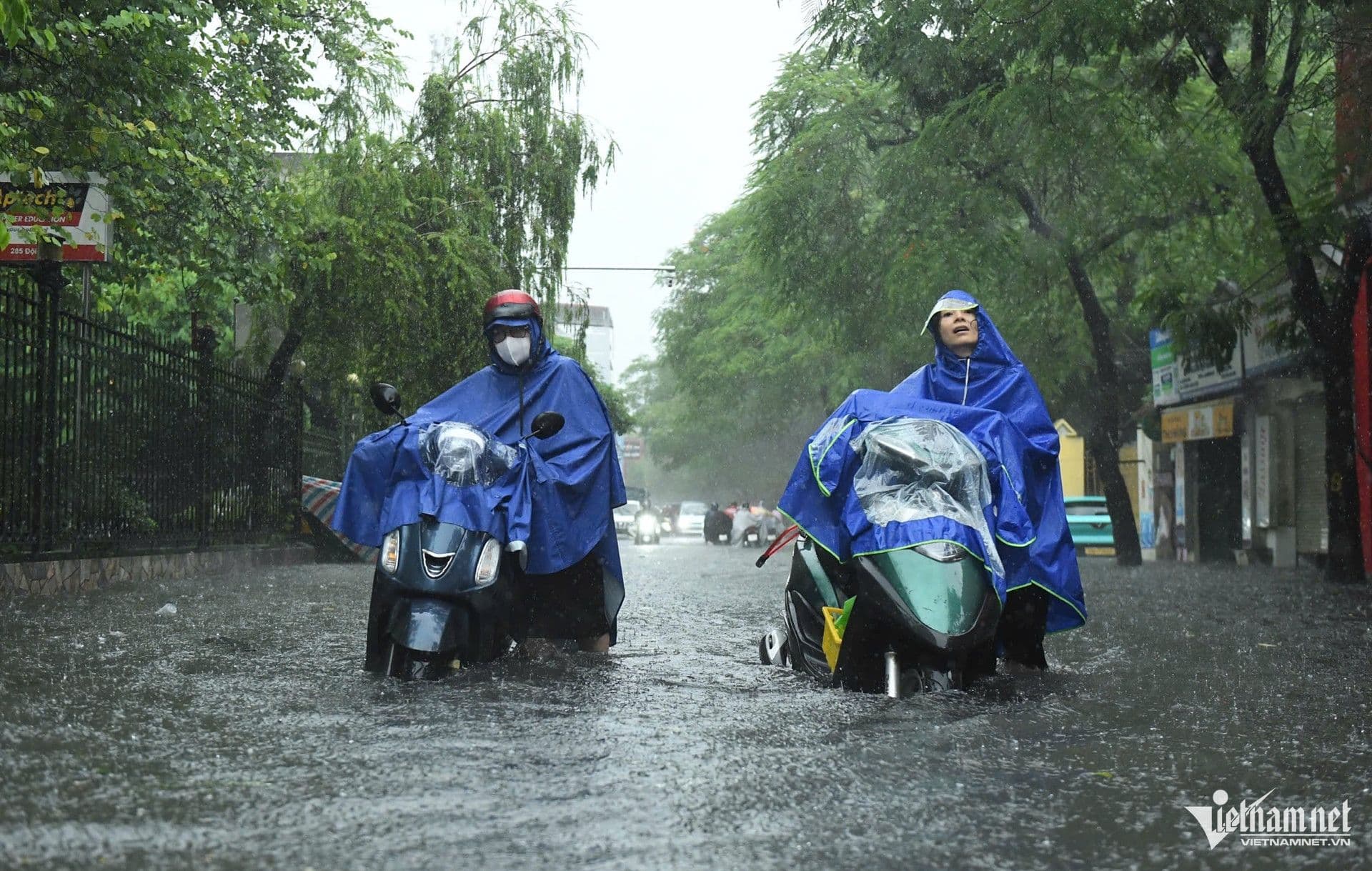 Người dân đi xe máy lội qua đường ngập nước trong cơn mưa lớn ở Hà Nội