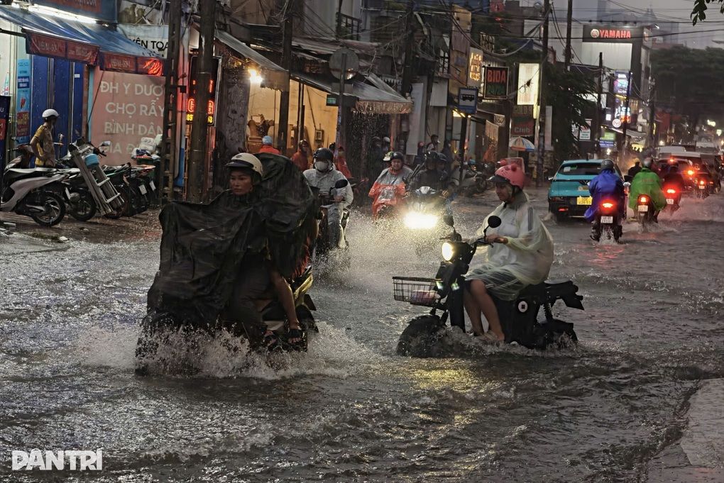 Người dân đi xe máy qua đường ngập lụt ở TPHCM trong trận mưa lớn, thể hiện tác động của biến đổi khí hậu đến đô thị.
