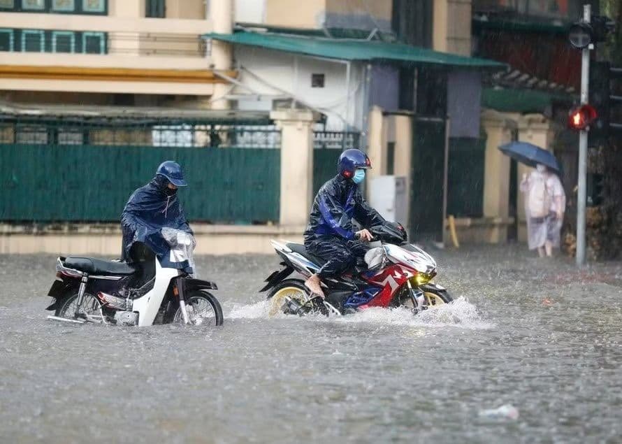 Người dân đi xe máy qua đường phố ngập lụt do mưa lớn ở Việt Nam, minh họa tác động của biến đổi khí hậu.