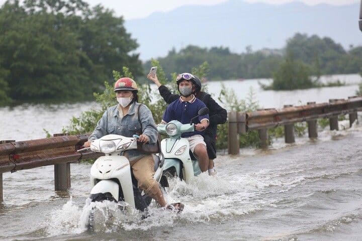 Người dân đi xe máy qua đoạn đường ngập sâu ở ngoại thành Hà Nội, thể hiện sự mong manh của hạ tầng giao thông trước biến đổi khí hậu