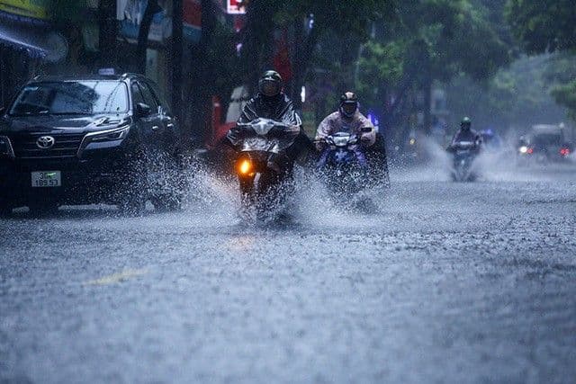 Người dân đi xe máy trên đường ngập nước do mưa lớn từ bão Ragasa, minh họa sự cần thiết của việc thích nghi.