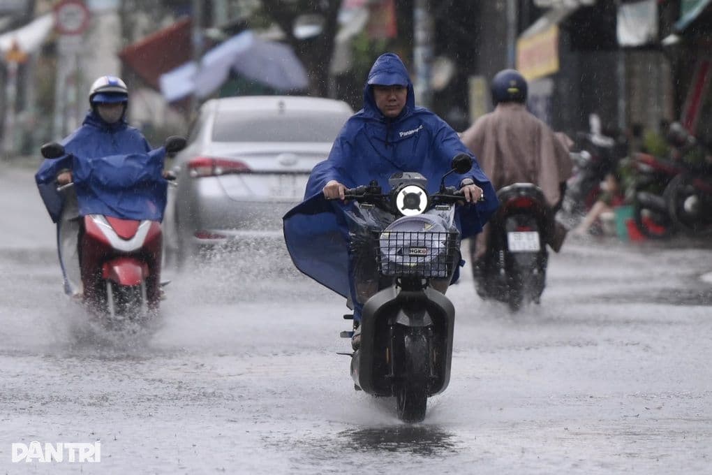 Người dân đi xe máy trong mưa lớn, nước ngập đường, thể hiện sự ảnh hưởng của thời tiết khắc nghiệt đến đời sống.