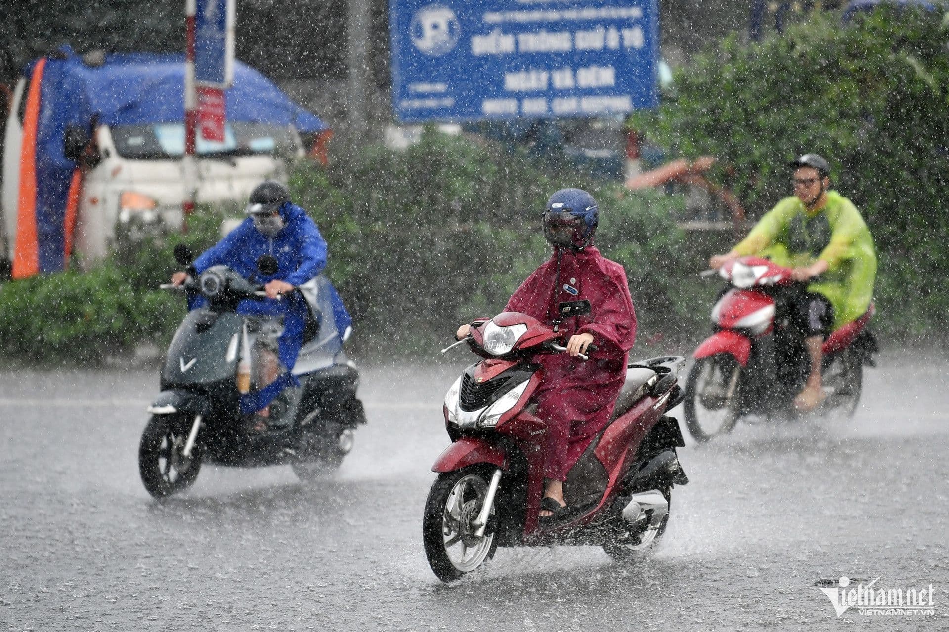 Người dân đi xe máy trong mưa lớn, thể hiện sự thích nghi với thời tiết khắc nghiệt.