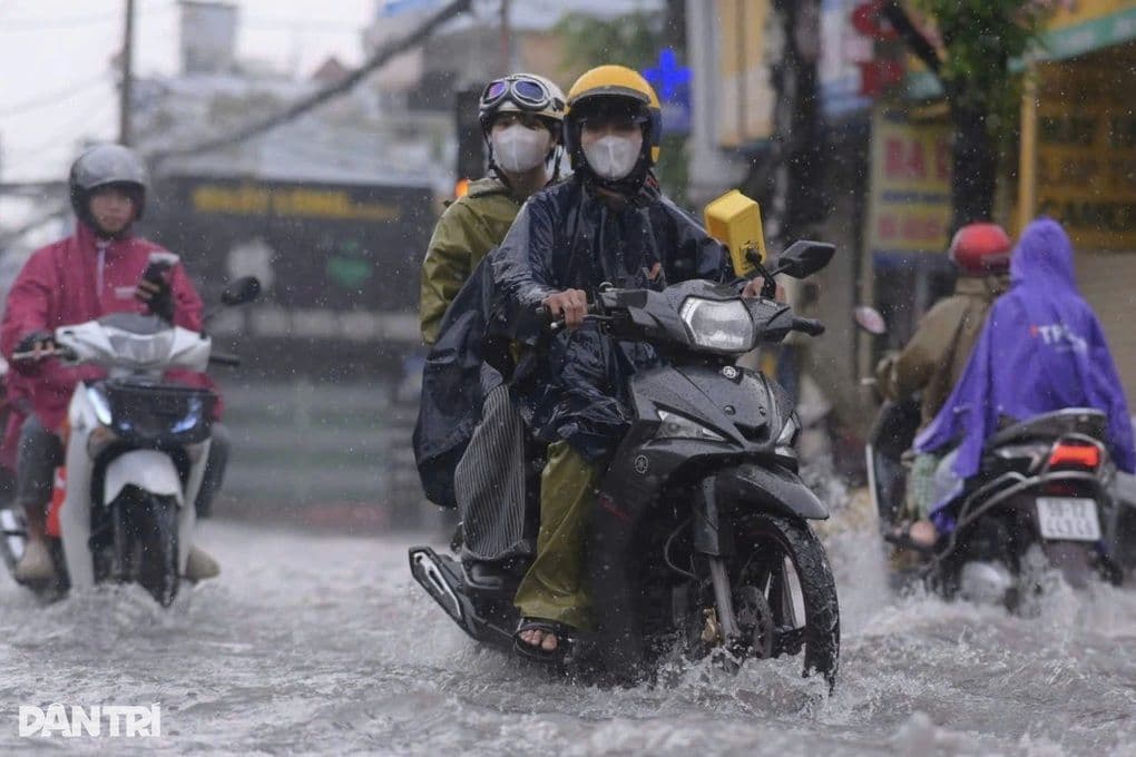 Người dân đi xe máy trong mưa lớn và đường ngập nước, minh họa tác động của thời tiết khắc nghiệt.