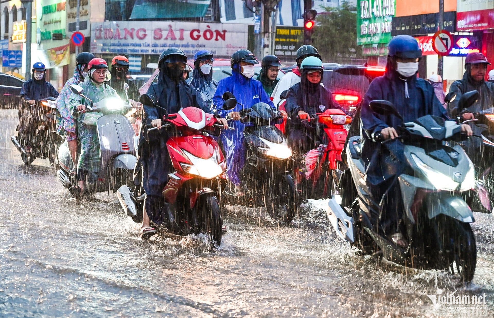 Người dân đi xe máy trong mưa lớn và đường ngập, nhấn mạnh tầm quan trọng của dự báo sớm và thích ứng với thời tiết khắc nghiệt.