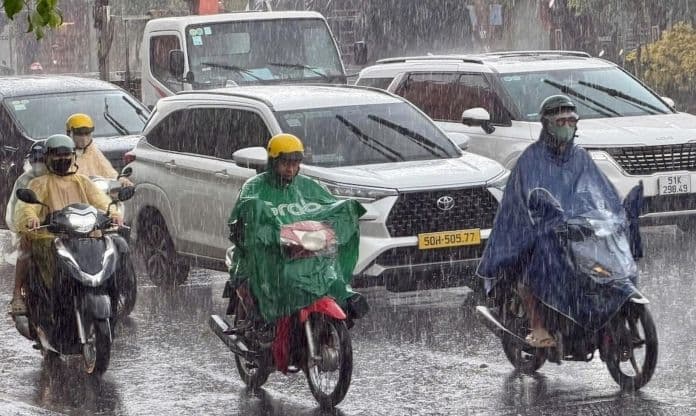 Người dân đi xe máy và ô tô dưới trời mưa lớn, thể hiện sự tương tác trực tiếp của con người với thời tiết.