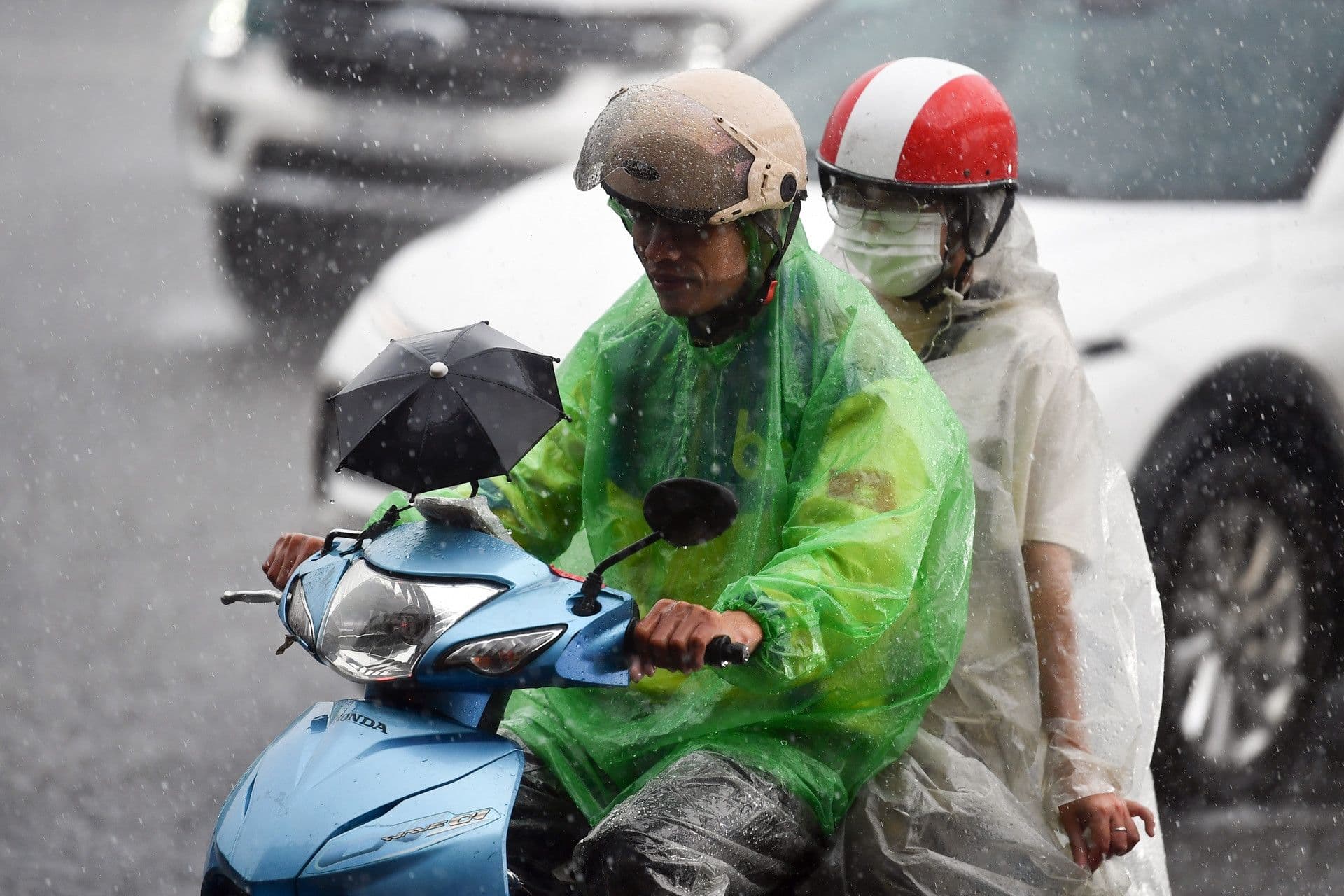 Người dân mặc áo mưa đi xe máy trong cơn mưa, thể hiện sự thích nghi với điều kiện thời tiết.