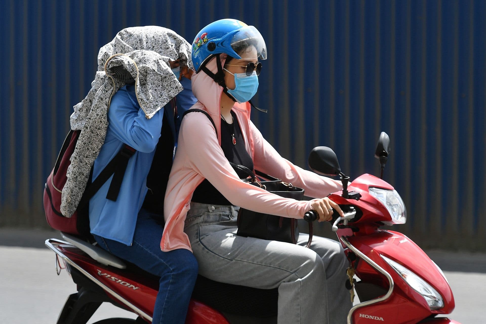 Người dân Sài Gòn che chắn nắng nóng khi di chuyển bằng xe máy, thể hiện sự gia tăng nhiệt độ đô thị.