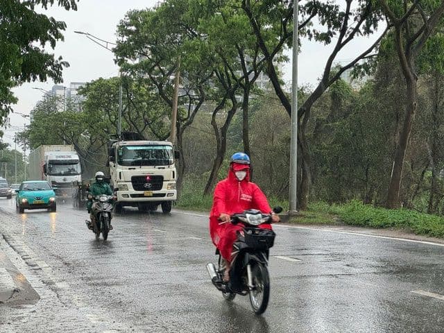 Người dân Sài Gòn đi xe máy trên đường ướt mưa, mặc áo mưa, thể hiện sự thích nghi với thời tiết đặc trưng của thành phố.