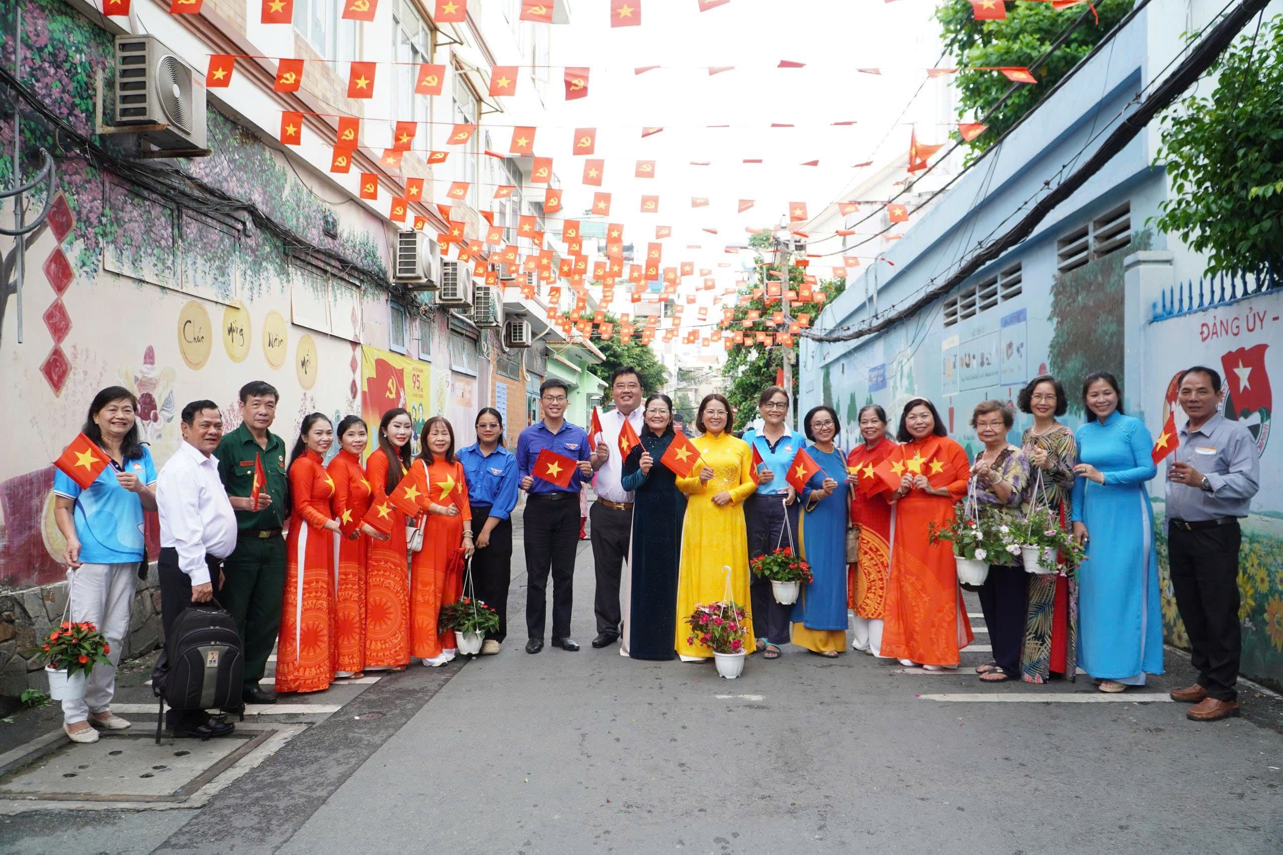 Người dân trong trang phục truyền thống đứng tại con hẻm được trang trí cờ Tổ quốc rực rỡ mừng Tết Độc lập