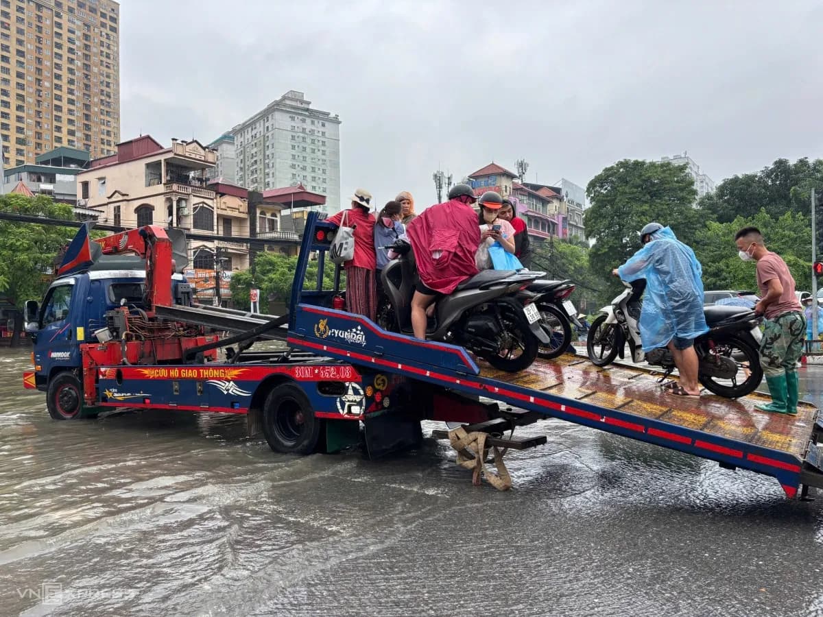 Người dân và đồng nghiệp hỗ trợ đẩy xe máy qua đoạn đường ngập sâu trên đường Phùng Hưng, Hà Đông, thể hiện nỗ lực ứng phó và giúp đỡ lẫn nhau trong tình hình mưa lũ.