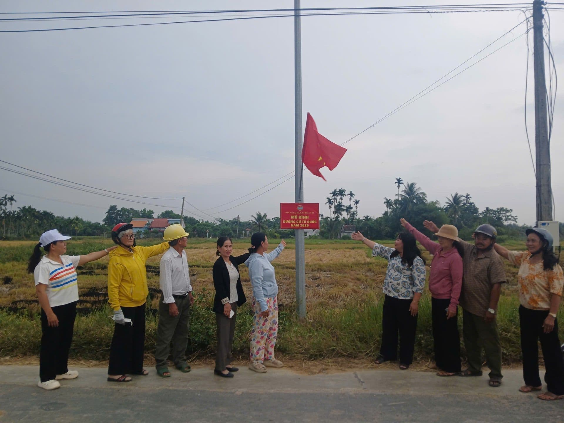 Người dân Việt Nam đứng bên đường làng với cờ Tổ quốc, tượng trưng cho khát vọng và sự phát triển từ nông thôn.