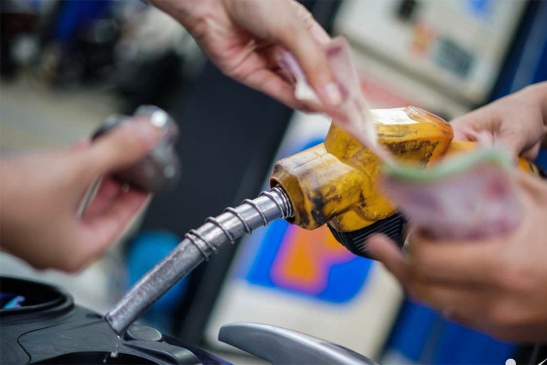 Người dân đổ xăng cho xe máy và trả tiền, minh họa gánh nặng chi phí xăng dầu tăng cao.